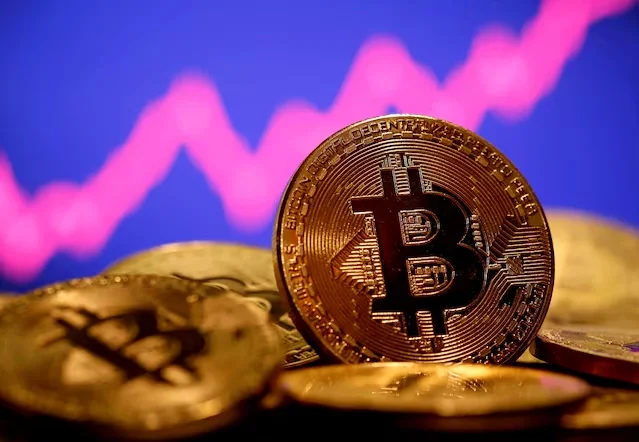 Đồng xu biểu trưng của Bitcoin được đặt trước màn hình đồ thị giá. Ảnh: Reuters