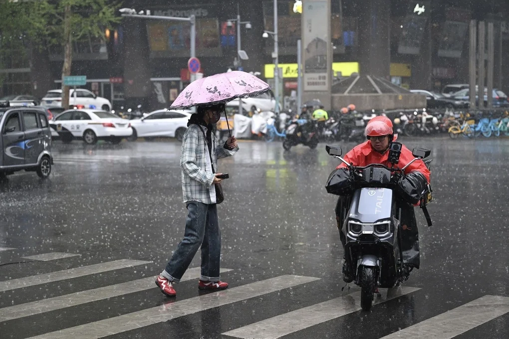 Người đàn ông đi xe máy lướt qua người phụ nữ đang cầm ô che mưa trên một con đường tại Bắc Kinh hôm 16/4. Ảnh: AFP